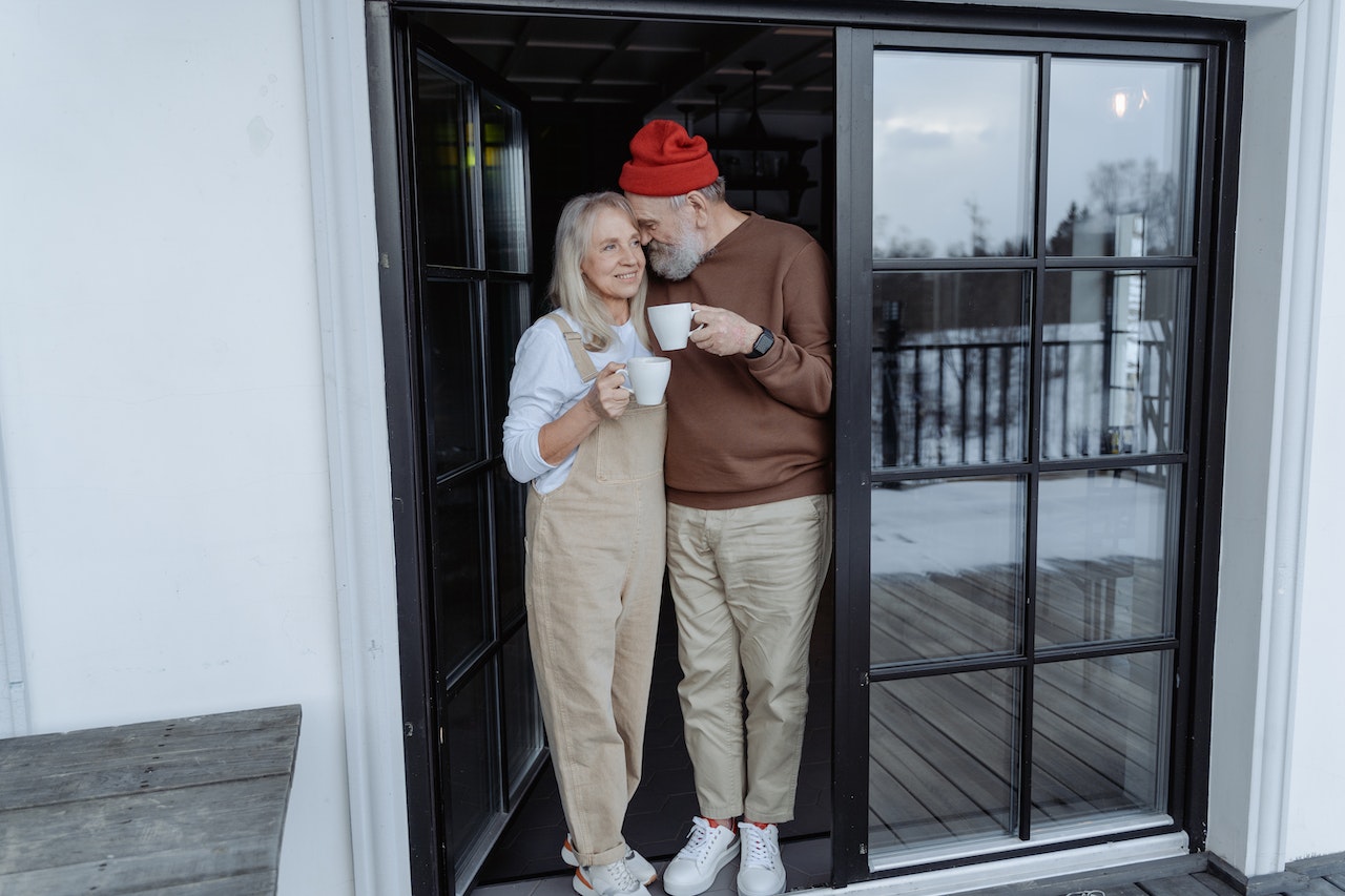 couple de seniors debout près de la porte avec des mugs